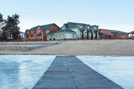 Winter village house on sandy beach near cold frozen river lake