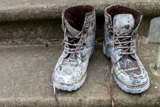 Old brown work boots. Boots smeared with white paint. Dirty boots on the stairs. Dirty old workboots on stairs.