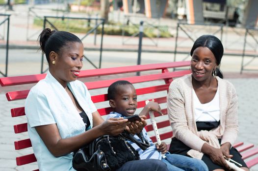 two young women sitting on a bench are talking with a little boy in the middle.