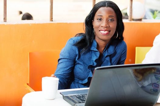 This beautiful young woman sitting at her laptop with a cup of coffee in front of her , smiling at the camera