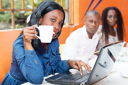 This beautiful smiling businesswoman, working on her laptop with a cup of coffee in hand.