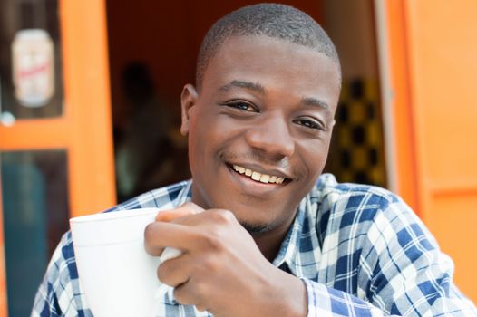 This happy young man holding a cup of coffee in hand.