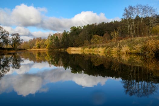 View on autumn landscape of river and trees in sunny day. Forest on river coast in autumn day. Reflection of autumn trees in water. Autumn in Latvia. Autumn landscape with colorful trees and river. 