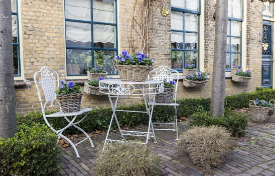 two old white metal chairs with a table and violets as flowers in a front garden in the Netherlands