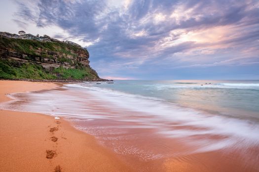 Waves wash up onto seashore washing away footprints left in the sand