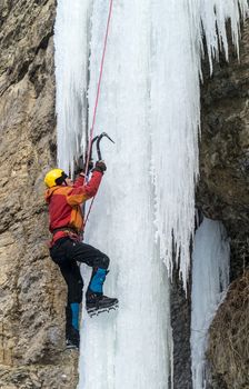 Extreme ice climbing. Man climbing the frozen waterfall using ice axes and crampons. Yellow alpine helmet