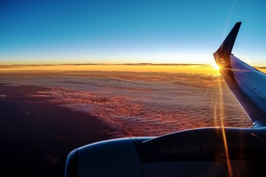 Sunset from a plain. View through the window of an aircraft. Wing of the plane above clouds.