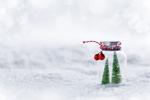 Christmas ornaments of glass jar with striped ribbon , bells and fir trees inside on snow background