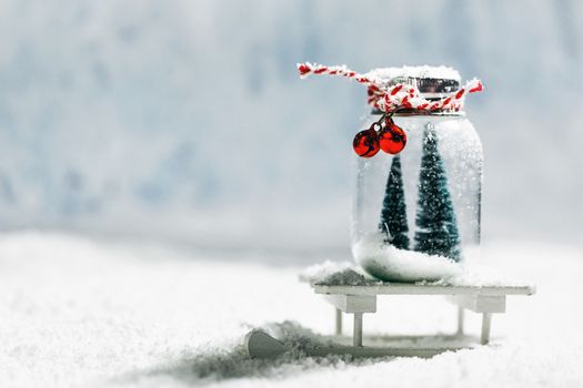 Christmas ornaments of glass jar with striped ribbon , bells and fir trees inside on snow background