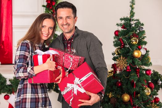 Couple in love sitting next to a nicely decorated Christmas tree, hloding Christmas gifts and smiling