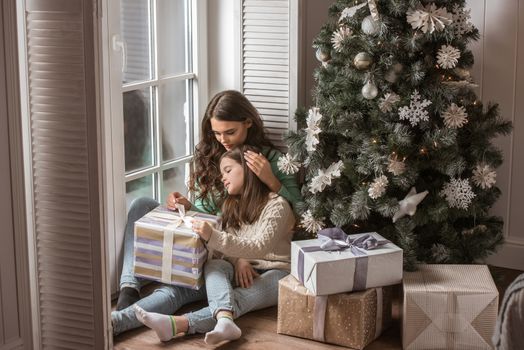 Mother and daughter unwrapping a gift sitting on the floor near christmas tree