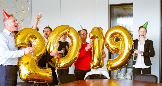 Business people celebrating 2019 New Year at office party holding golden balloons