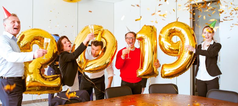 Business people celebrating 2019 New Year at office party holding golden balloons