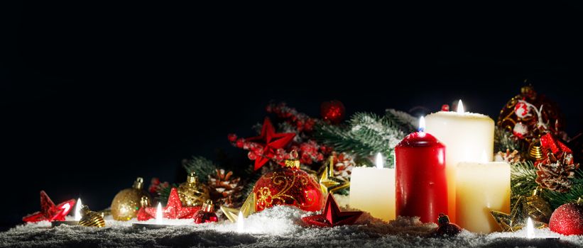 Burning christmas candles with red and golden decorative stars , baubles , pine cones and green branches on snow