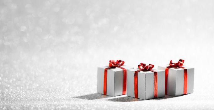Small decorative Christmas gift boxes with red ribon bows on silver glitter background with copy space