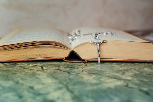 Silver rosary and cross with jesus on the Bible on a green table. Religion at school,vintage style.