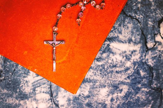 Silver rosary and cross resting on the closed book at gray table, seen from above.religion school concept.Vintage style.