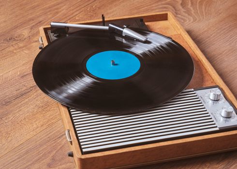 Older Gramophone with a vinyl record on wooden table,vintage style.