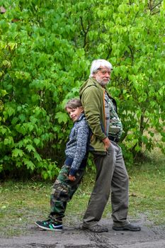 Happy grandfather and boy have fun and play in park on beautiful sunny day. Senior and child in Kemeri National park, Latvia. Happy senior and boy in green park.