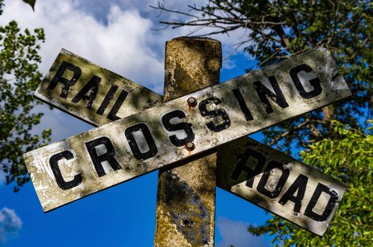 Railroad crossing sign with blue sky background with clouds.