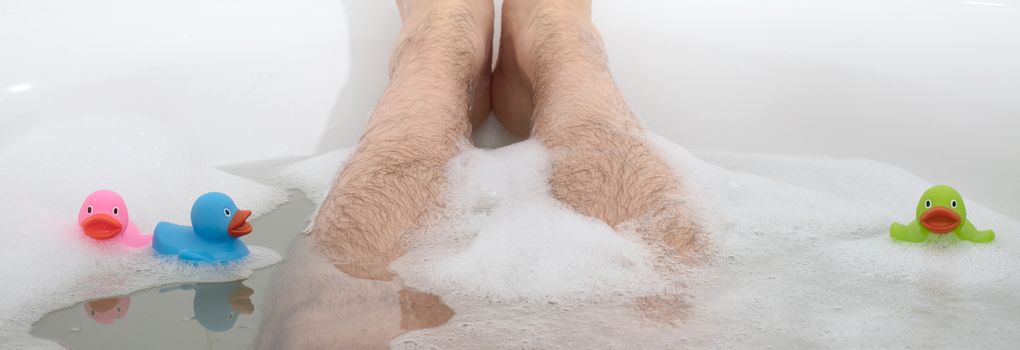 Men's feet in a bright white bathtub, selective focus on toes