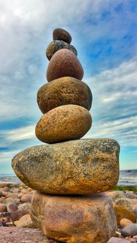 Pyramid of stones on the beach, against a blue sky with white clouds