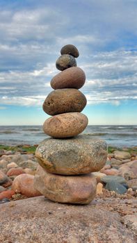 Pyramid of stones on the beach, against a blue sky with white clouds