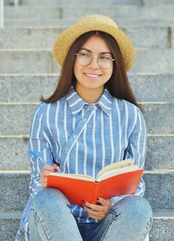 Portrait of a young Asian student in glasses with a hat dressed in a blue striped shirt that writes tasks and looks into the distance.Vertical photography