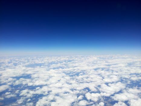 top view of white clouds from a airplane, on a background of the clear blue sky.