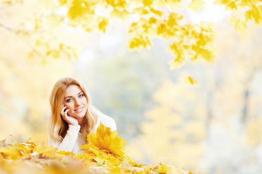 Beautiful young woman laying on yellow leaves in autumn park