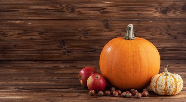 Autumn harvest still life with pumpkins , apples and hazelnuts on wooden background