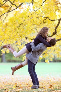 Smiling mid adult couple hug in autumn forest of yellow maple trees