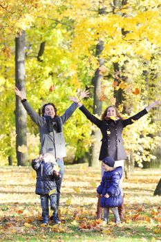 Happy family playing with autumn maple leaves in park at sunny day