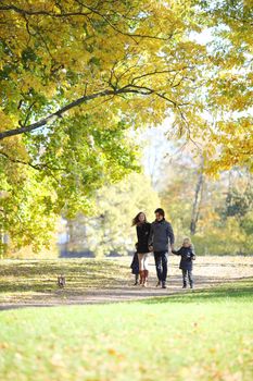 Happy family with two children walking in sunny autumn park holding hands