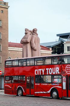 Riga sightseeing bus tour on the Latvian Riflemen Square Latvia. Latvian Riflemen monument behind the tourist bus. Riga city view with tourist bus. Tourist bus in downtown Riga.