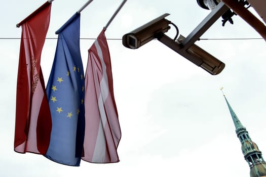 Latvian and European flags and camcorder on the background of sky. Flags, video camera and St. Peter's Church in Riga, Latvia.
