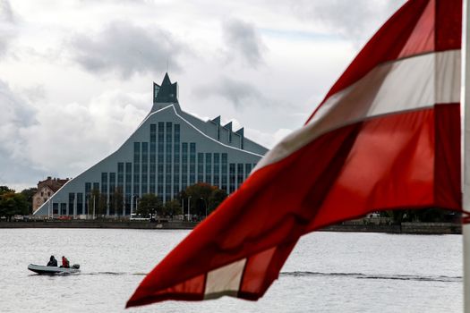 Latvian National Library. Cityscape from November 11 embankment with Latvian National Library, Latvia flag and motor boat in Riga. River Daugava and National Library. National Library in center of Riga.