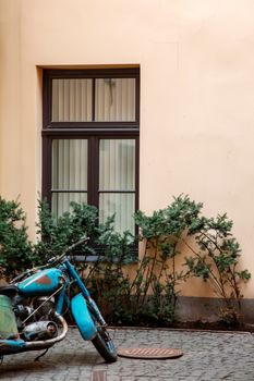 Fragment of beige wall with window in Old Riga, Latvia. Ancient motorcycle next to the wall.