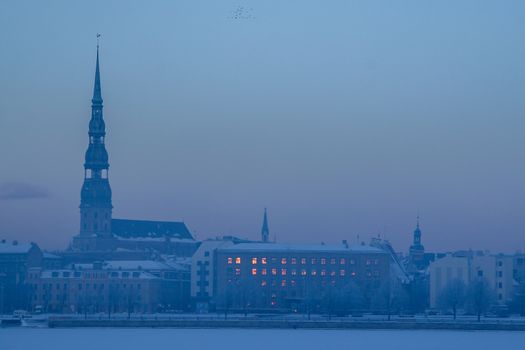 Riga view in winter; Riga, capital city of Latvia in winter time. View of St Peter's Church in winter. View of Old Riga with frozen river Daugava in the foreground. City Riga with background of blue sky. 