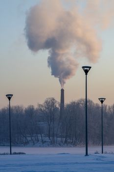 Riga view in winter; Riga, capital city of Latvia in winter time. View of Riga with frozen river Daugava and smoky chimney. City Riga with background of blue sky. 