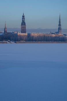 Riga view in winter; Riga, capital city of Latvia in winter time. View of St Peter's Church, St. Jacob's Cathedral and Anglican Church. View of Old Riga with frozen river Daugava in the foreground. City Riga with background of blue sky. 
