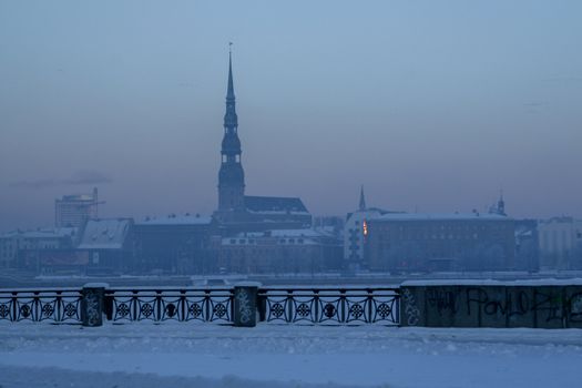 Riga view in winter; Riga, capital city of Latvia in winter time. View of St Peter's Church in winter. View of Old Riga with frozen river Daugava in the foreground. City Riga with background of blue sky. 