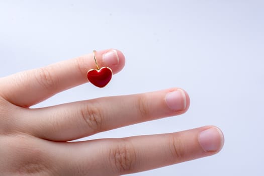 Red color heart shape earring in hand on white