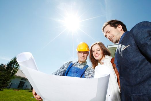 Worker shows house design plans to a young couple at construction site