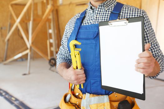 Worker with a monkey wrench and clipboard at construcion site