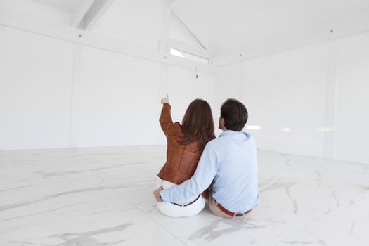 Young couple sitting on the floor of new empty house and pointing up into the air