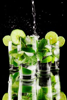 Pouring fresh mojito cocktail in glasses isolated on black background