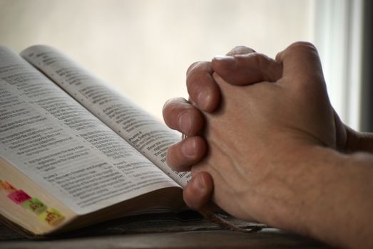 Man holding his hands close to the bible and praying.