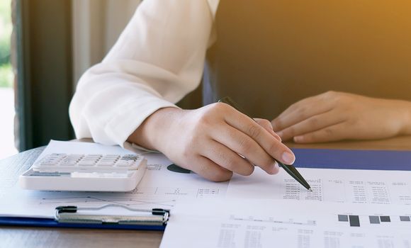 Businesswoman analyzing investment charts and pressing calculator buttons over documents. Accounting Concept