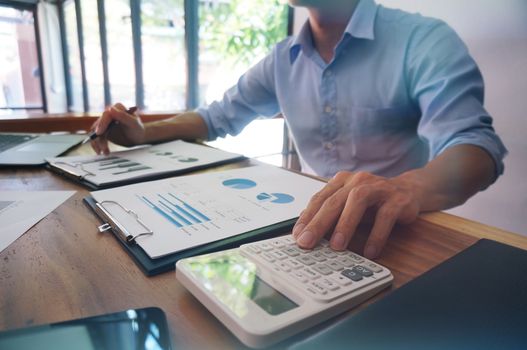 Businessman analyzing investment charts and pressing calculator buttons over documents. Accounting Concept.